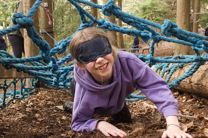 Girl crawling under cargo net wearing a blindfold and smiling