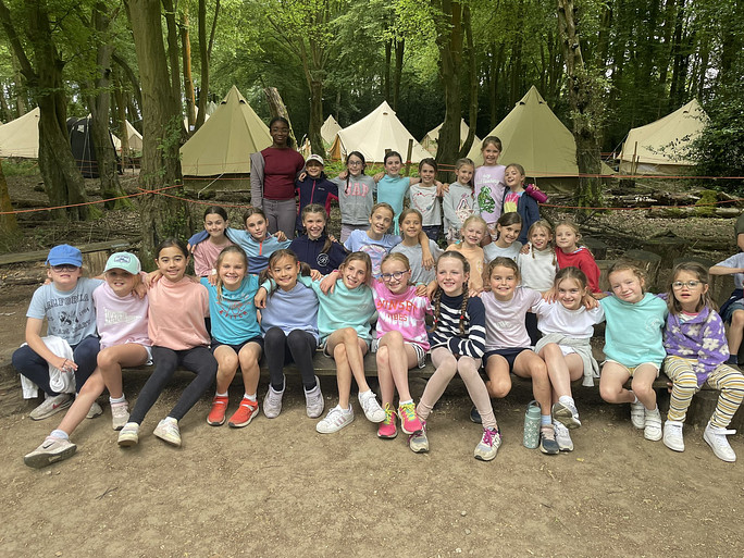 Young girls sitting with their arms around each other and smiling with tents in the background